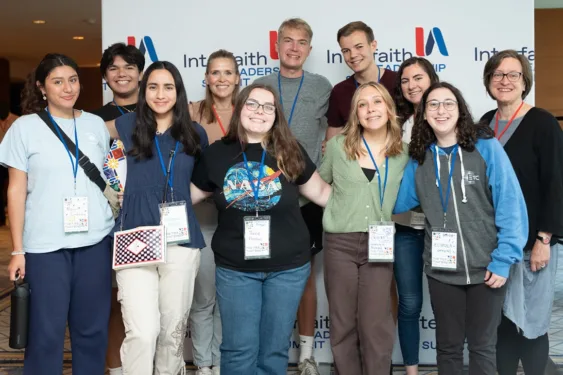 A group of students and staff wearing conference lanyards pose for a group photo in front of an “Interfaith Leadership Summit” backdrop.