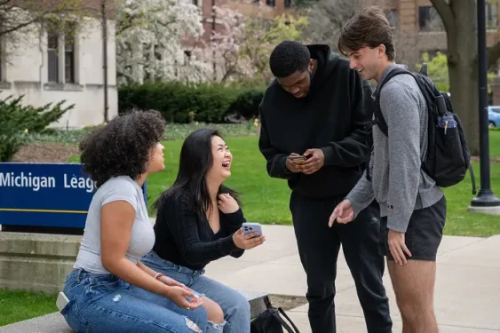 Four students in conversation with two sitting and two standing outside of the Michigan League in Ann Arbor, MI