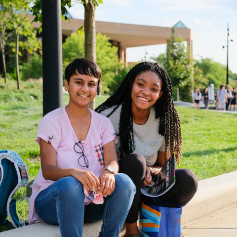 Two students sit beside a grassy lawn during an event on North Campus. 