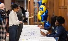 Two students seated at a welcome table assist a third student