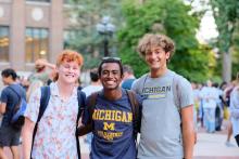 Three students smile in the middle of the Diag on a warm day in late summer.