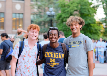 Three students smile at camera in front of a busy Diag