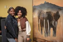Elsa Olander and friend smiling next to her painting of three elephants at the Ambatana Hallway Celebration