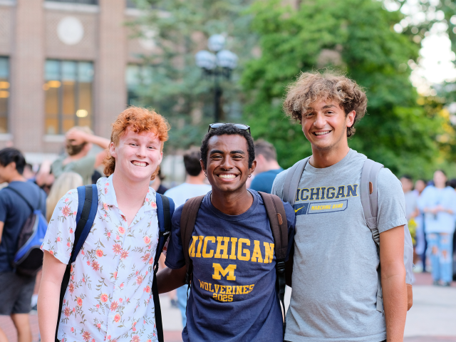 Three students smile at camera in front of a busy Diag