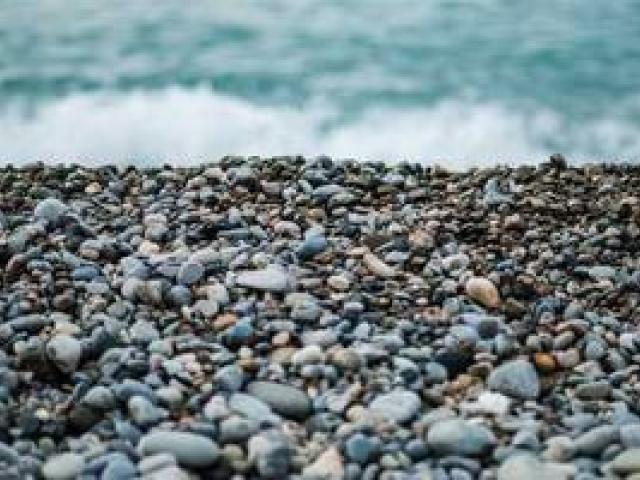 A close-up image of multi-colored rocks on a beach. In the background, you see waves crashing onto the rocks.